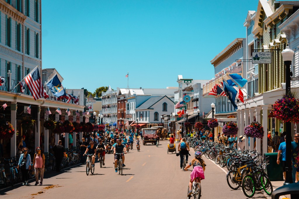 old timey storefronts with flags waving and people riding bicycles