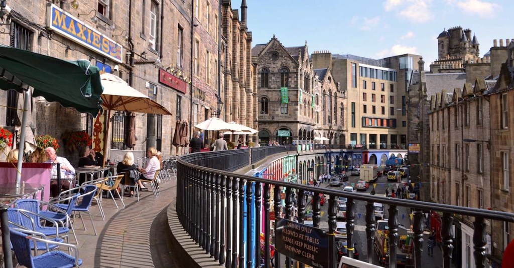 A row of cafe tables along a balcony walkway, overlooking a busy street.